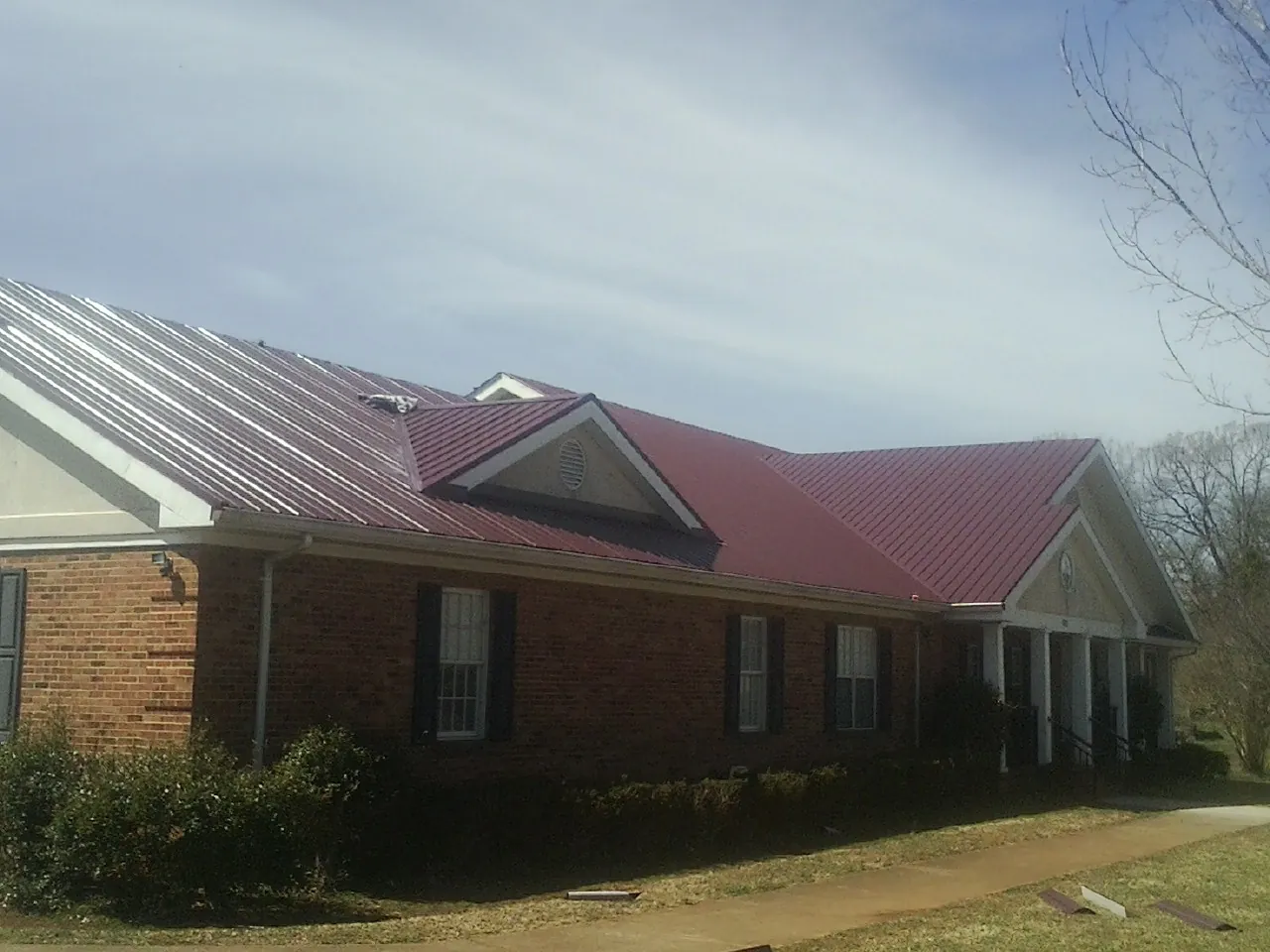 Red metal roof with gabled entries on a long brick building, from a Hail Damage Roof Repair job in Gretna