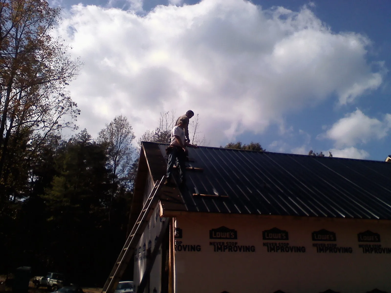 Roofer fastening dark metal panels high against a cloudy sky, from a Roof Inspection job in Gretna