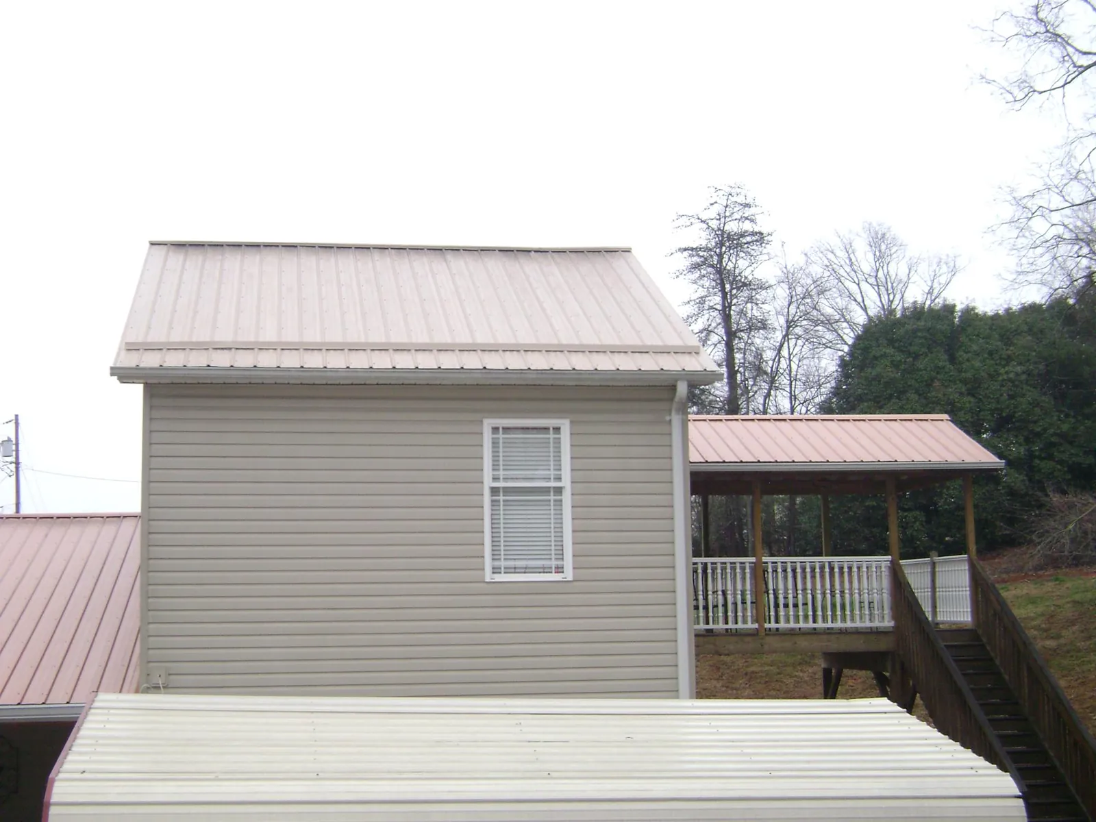 Tan metal roofs on a two story addition and attached porch, from a Roof Replacement job in Gretna